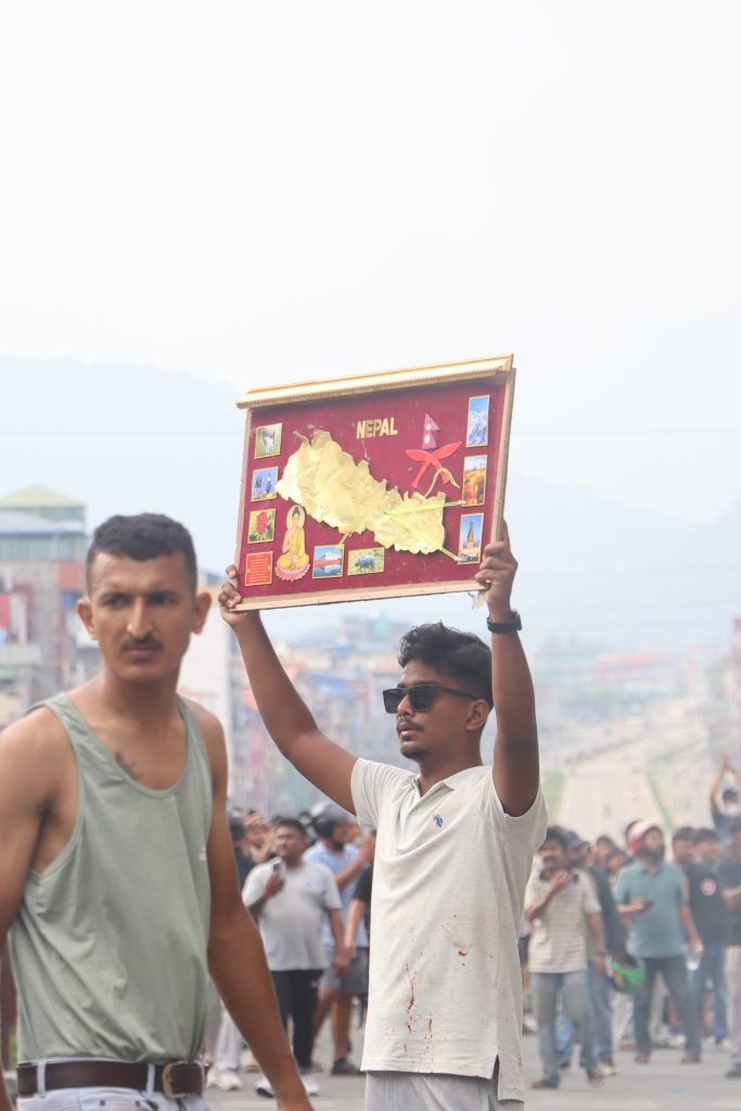 A young protester holds a framed map of Nepal above a crowd filling a city road